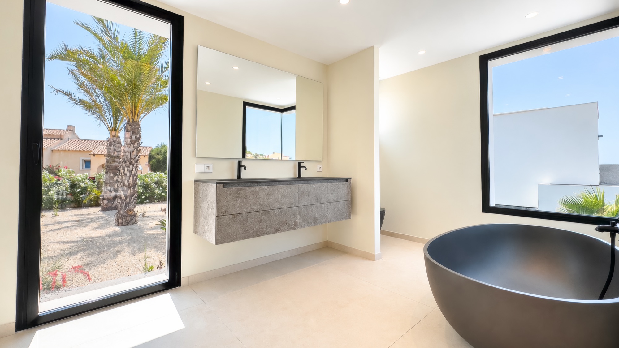 Main bathroom with freestanding black stone bath, stone vanity and palm view