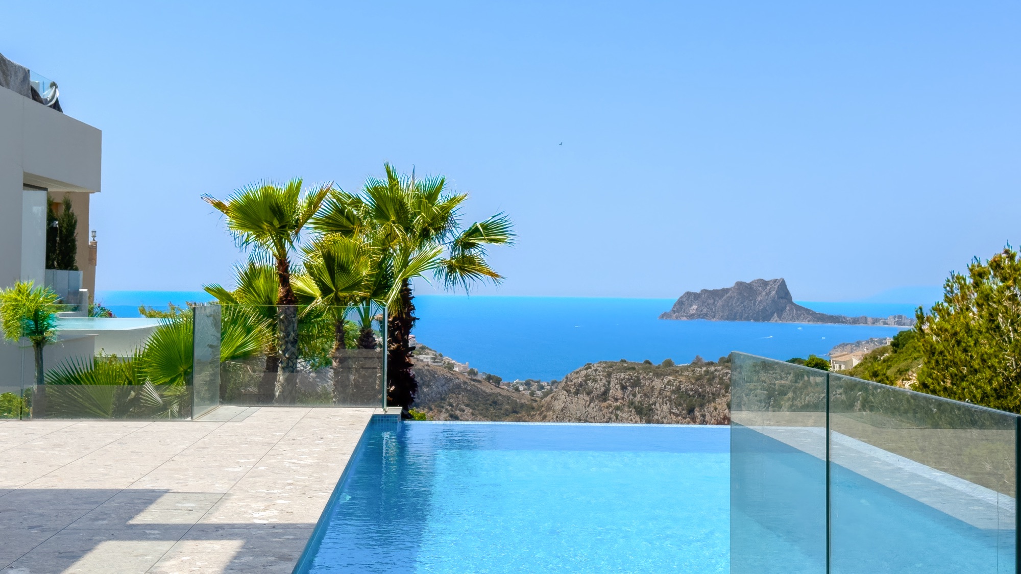 Corner of the infinity pool with a palm and the Penon de Ifach across the water