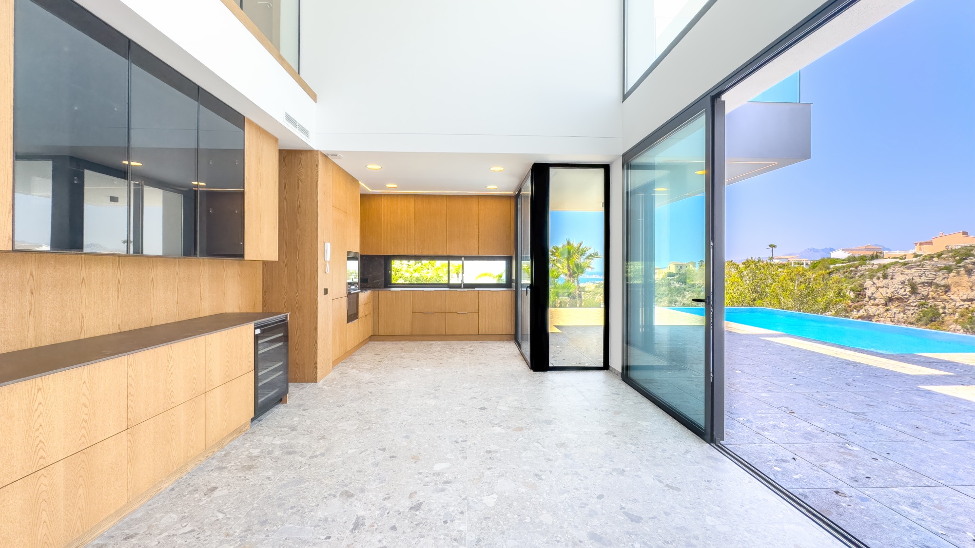 Kitchen with full-height oak joinery under the double-height void, glass wall open to the infinity pool